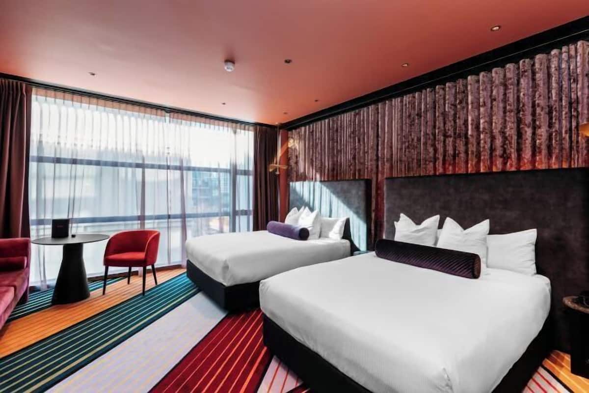 A hotel room with two beds, a sofa, a small table, and a large window.