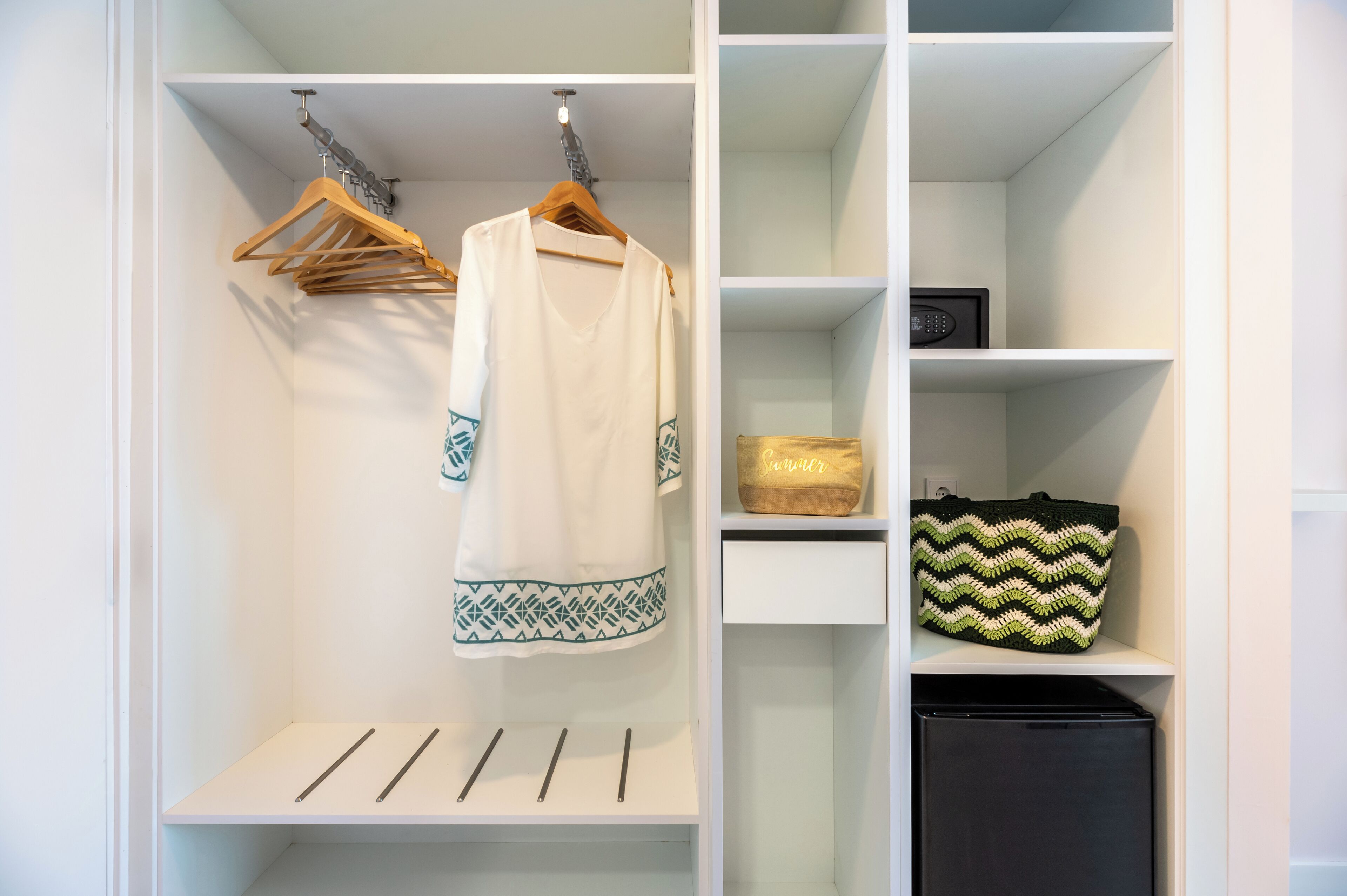 A white closet with shelves, a hanging rack, and a black storage unit.