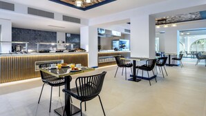 Ein modernes Restaurant mit einer zentralen Theke, schwarzen Stühlen und einer Decke mit geometrischem Muster.