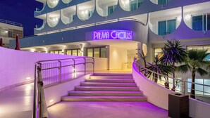 Ein Hotel Eingang mit einem Neon-Schild mit der Aufschrift "PALMA CACTUS", einer Treppe und Palmen.