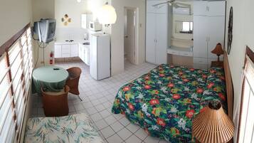A compact bedroom with a bed, a small kitchenette, a TV, and a ceiling fan.