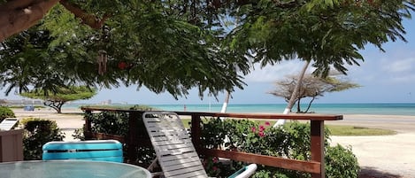 A beachside patio with a table and chairs, overlooking a sandy beach and turquoise waters.