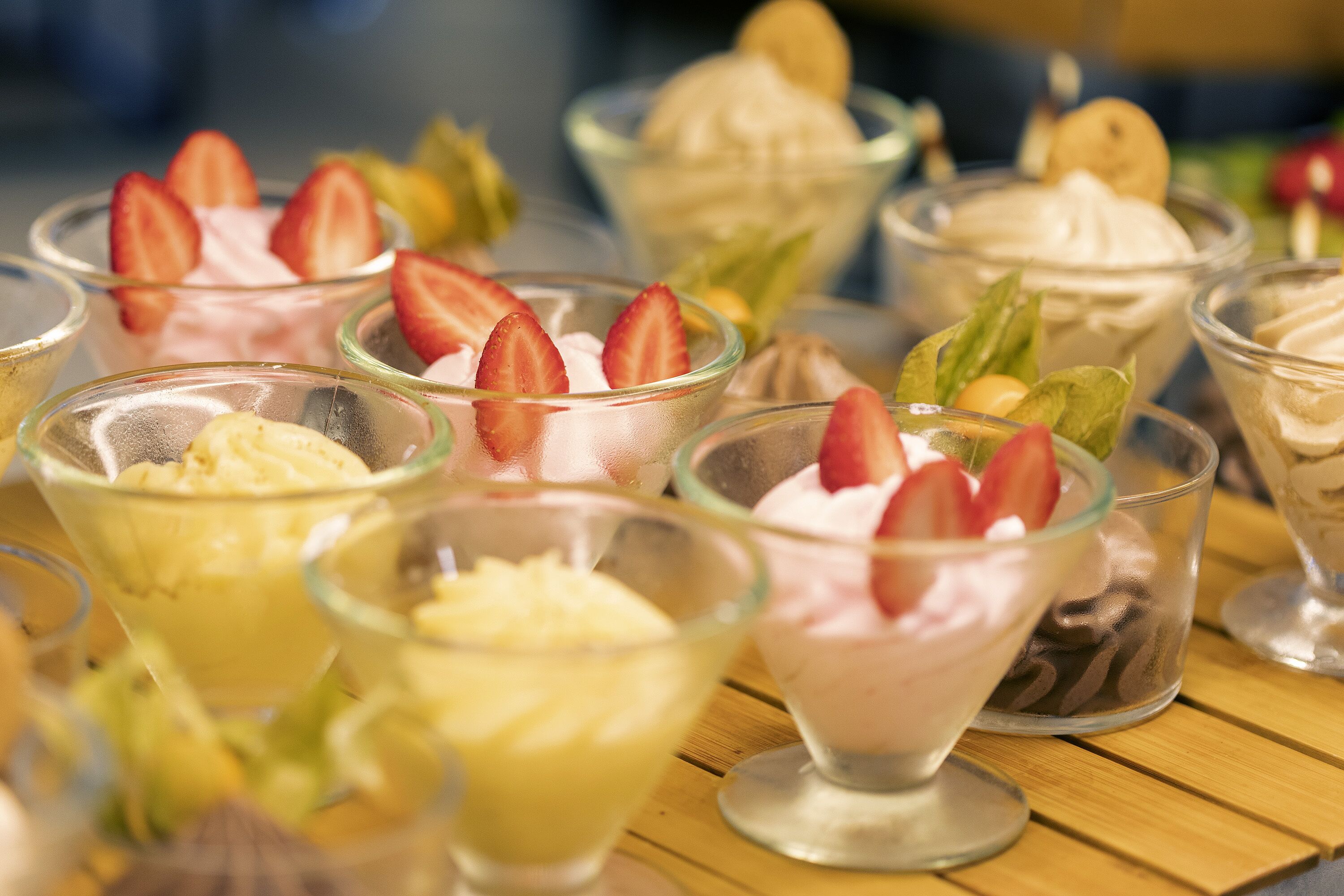 Diversos postres de helado en vasos de vidrio transparente, cada uno decorado con distintas frutas y adornos.