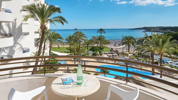 Un balcón con mesa, sillas y vistas a una piscina y playa.