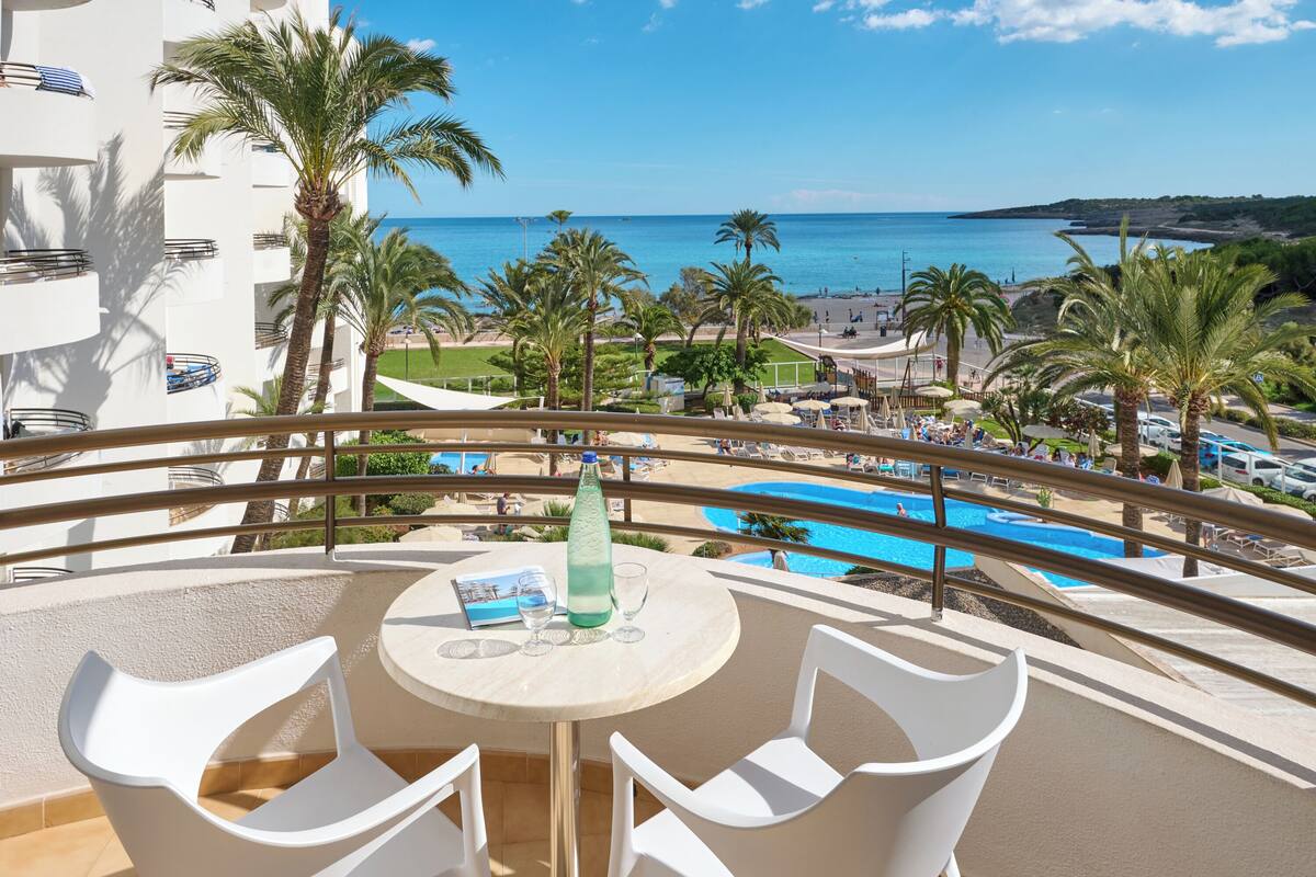 Een balkon met een tafel, stoelen en uitzicht op een zwembad en strand.