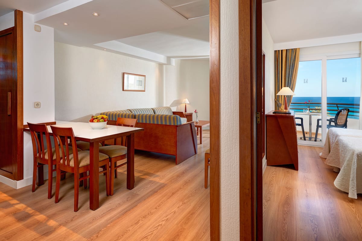 Een hotelkamer met een eethoek, een bank, een bed en een balkon met uitzicht op zee.
