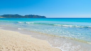 Una playa con agua turquesa cristalina, una orilla arenosa y una montaña al fondo.