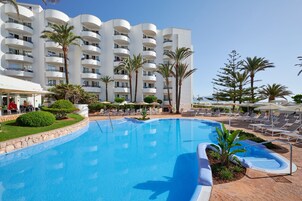 Un hotel con una piscina grande, palmeras y tumbonas.