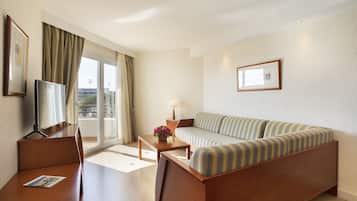 A hotel room with a wooden bed, a sofa, a desk, and a TV.