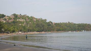 Una playa con barcos y una persona vadeando en el agua.