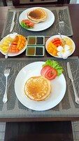 A table set with plates of pancakes, fresh fruit, and condiments.