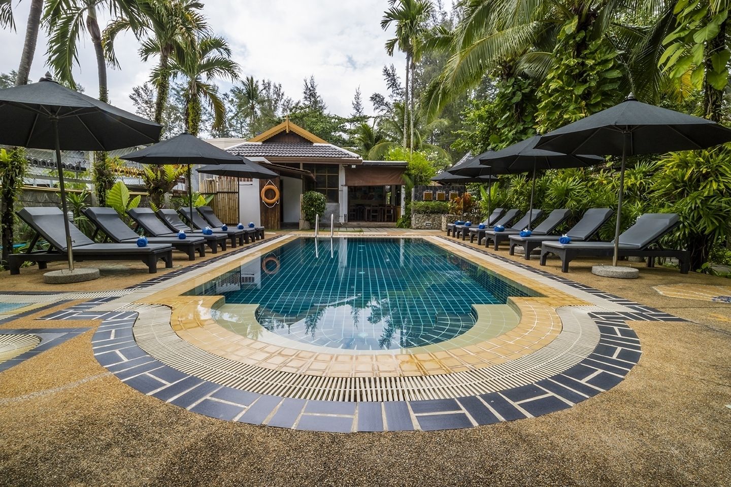 Une piscine entourée d’une végétation tropicale, avec des chaises longues et des parasols.