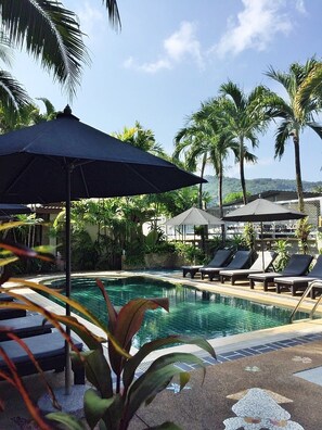 A poolside area with lounge chairs and umbrellas, surrounded by palm trees and a clear sky. - Bangtao Beach Chalet (Choeng Thale)