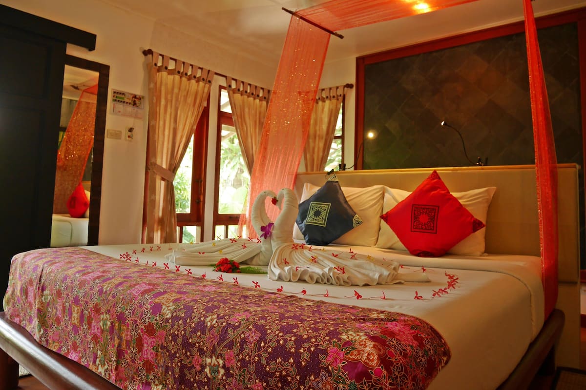 A bed with a floral bedspread, a decorative swan pillow, and a red pillow.