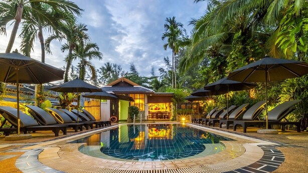 A pool area with lounge chairs and umbrellas, surrounded by palm trees and a bar. - Bangtao Beach Chalet (Choeng Thale)