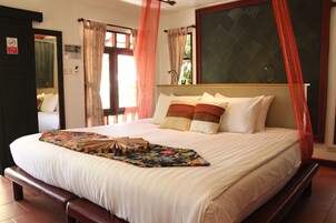 Una cama bien hecha con una colcha estampada con motivos florales, cabecera de madera y ventana con cortinas.