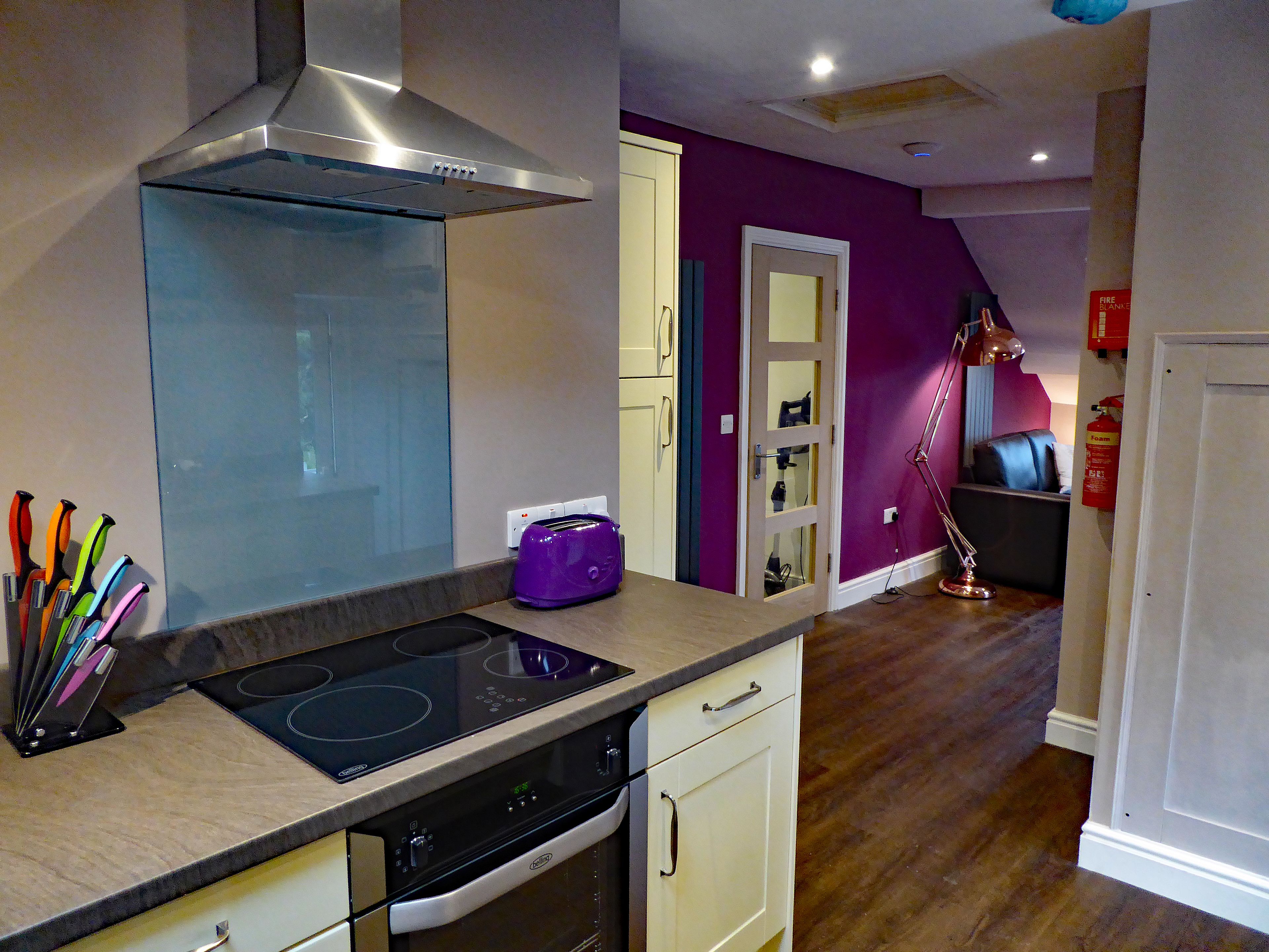 Una cocina con una campana extractora de acero inoxidable, un tostador morado y un juego de cuchillos de colores sobre la encimera.
