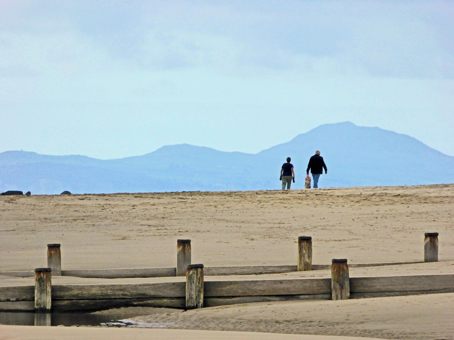 A beach with a wooden walkway leading to a mountain in the background.