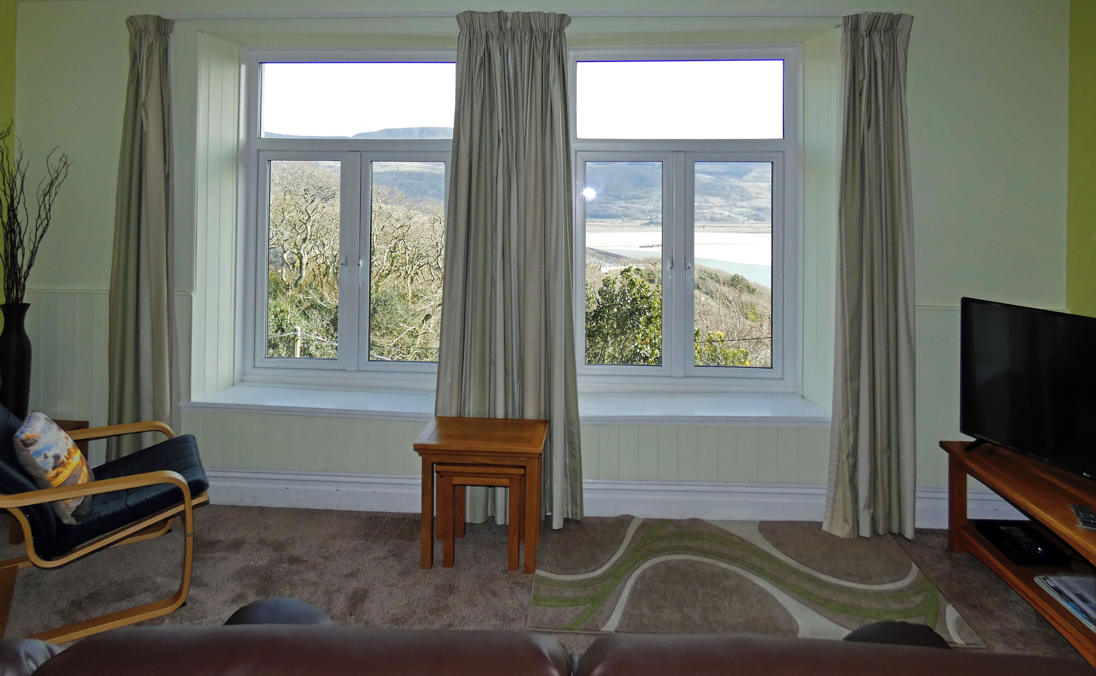 A living room with a large window, a television, a chair, and a small table.