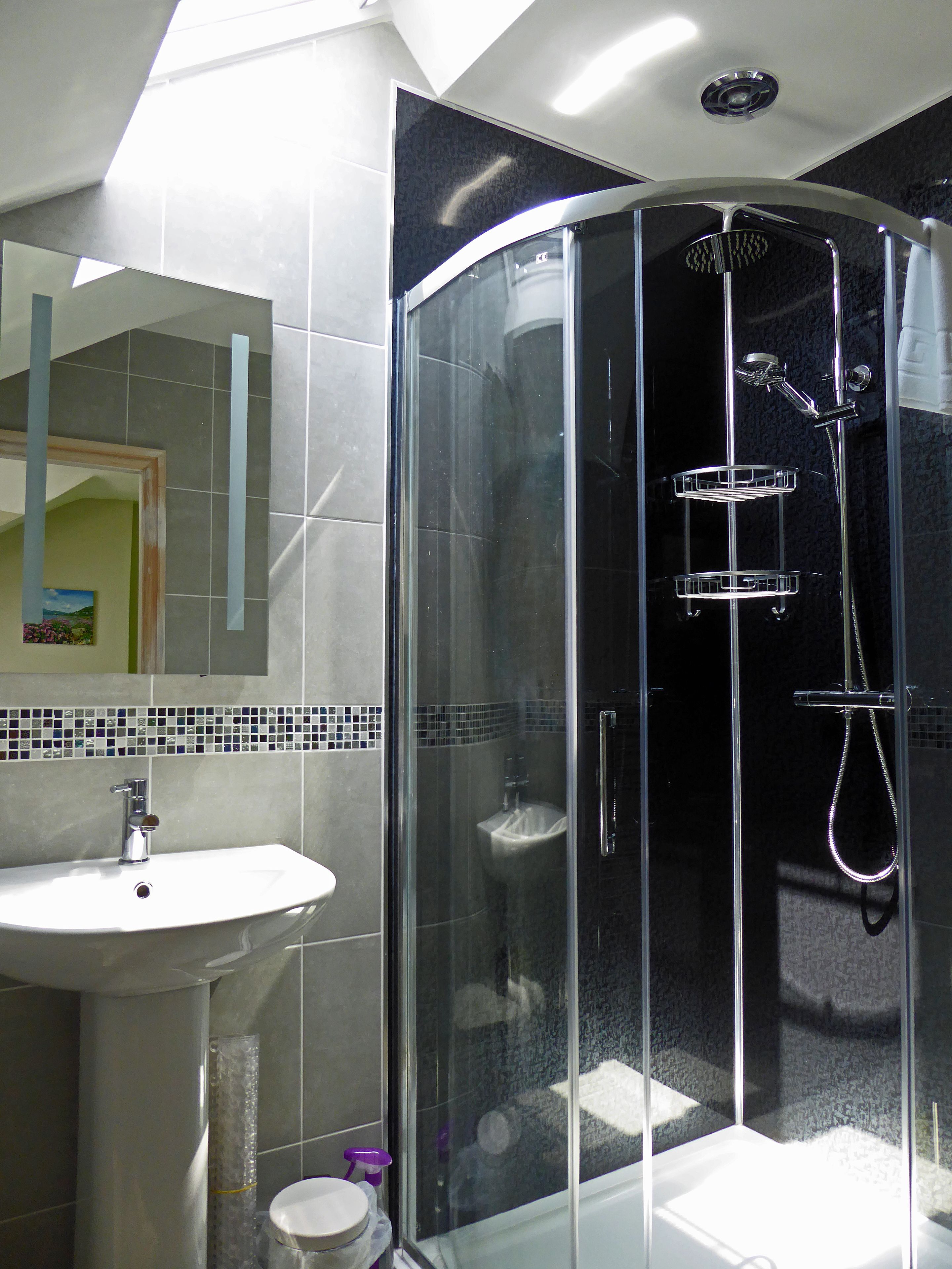 Un baño moderno con ducha envuelta en vidrio, lavamanos pedestal y salpicadero de azulejos.