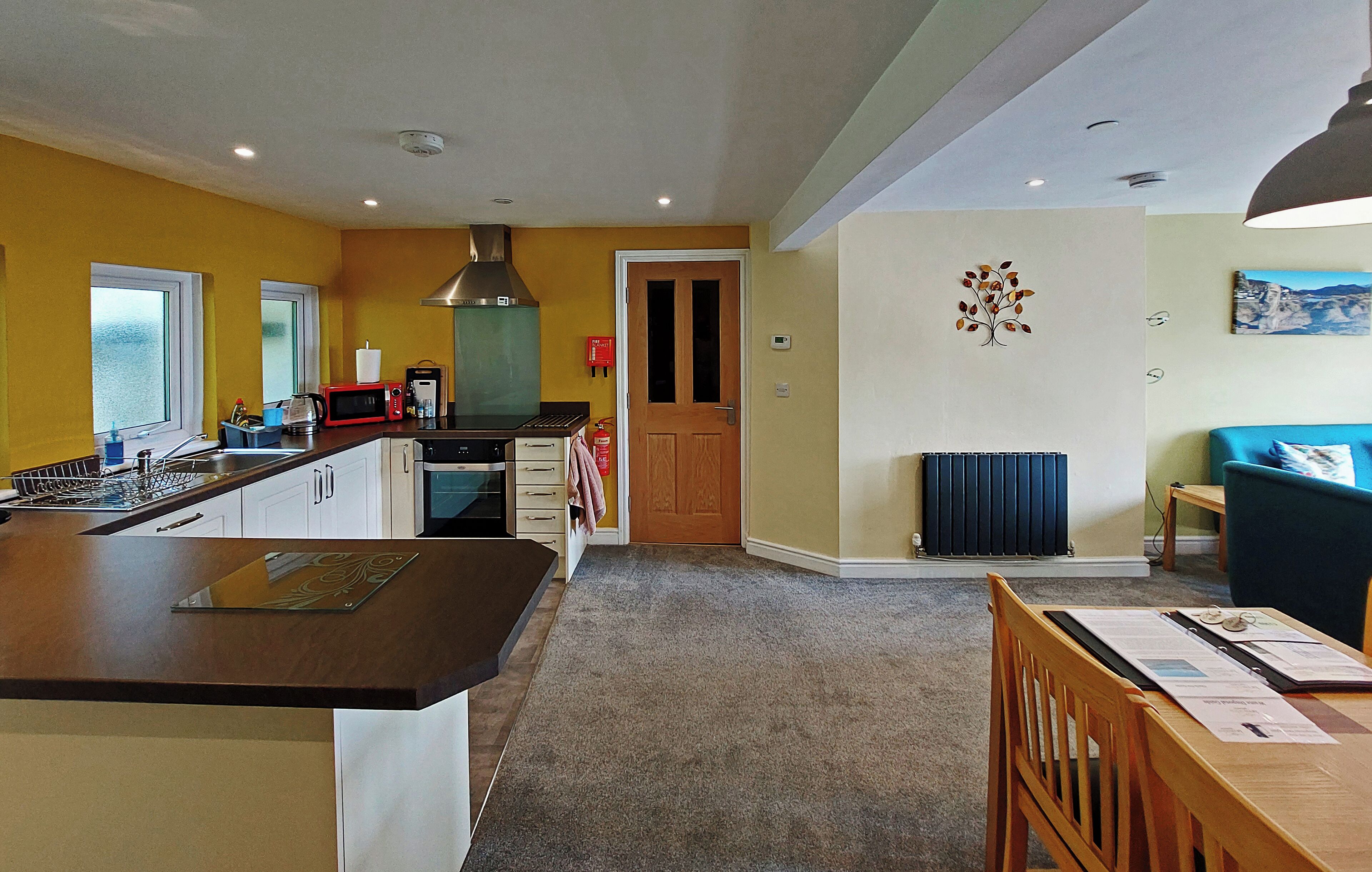 Uma cozinha moderna com uma ilha central, uma área de refeições com mesa e cadeiras, e um espaço de estar com um sofá e um quadro na parede.