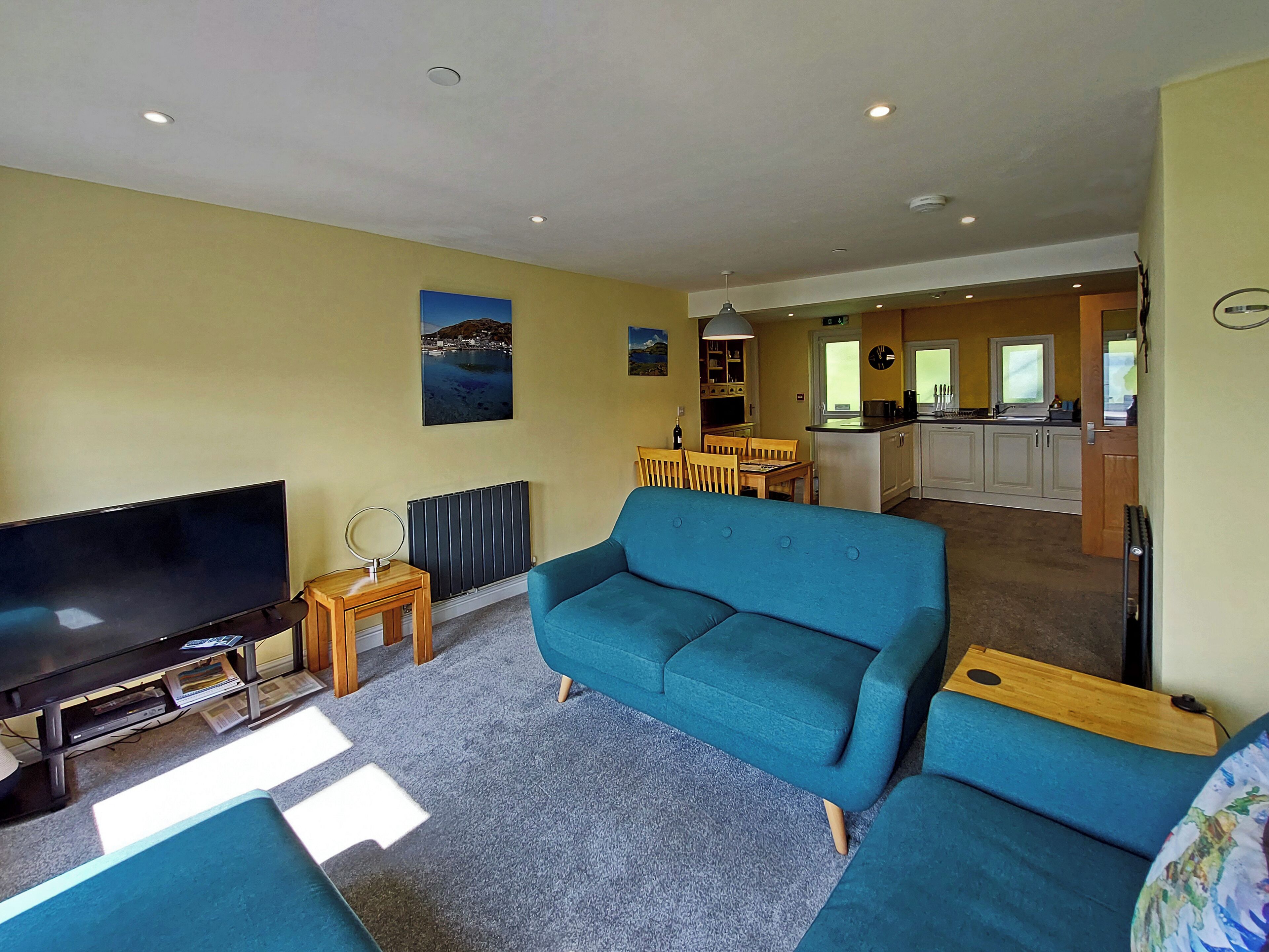 A living room with a large flat-screen TV, a blue sofa, and a small wooden side table.