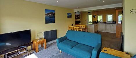 A living room with a large flat-screen TV, a blue sofa, and a small wooden side table.