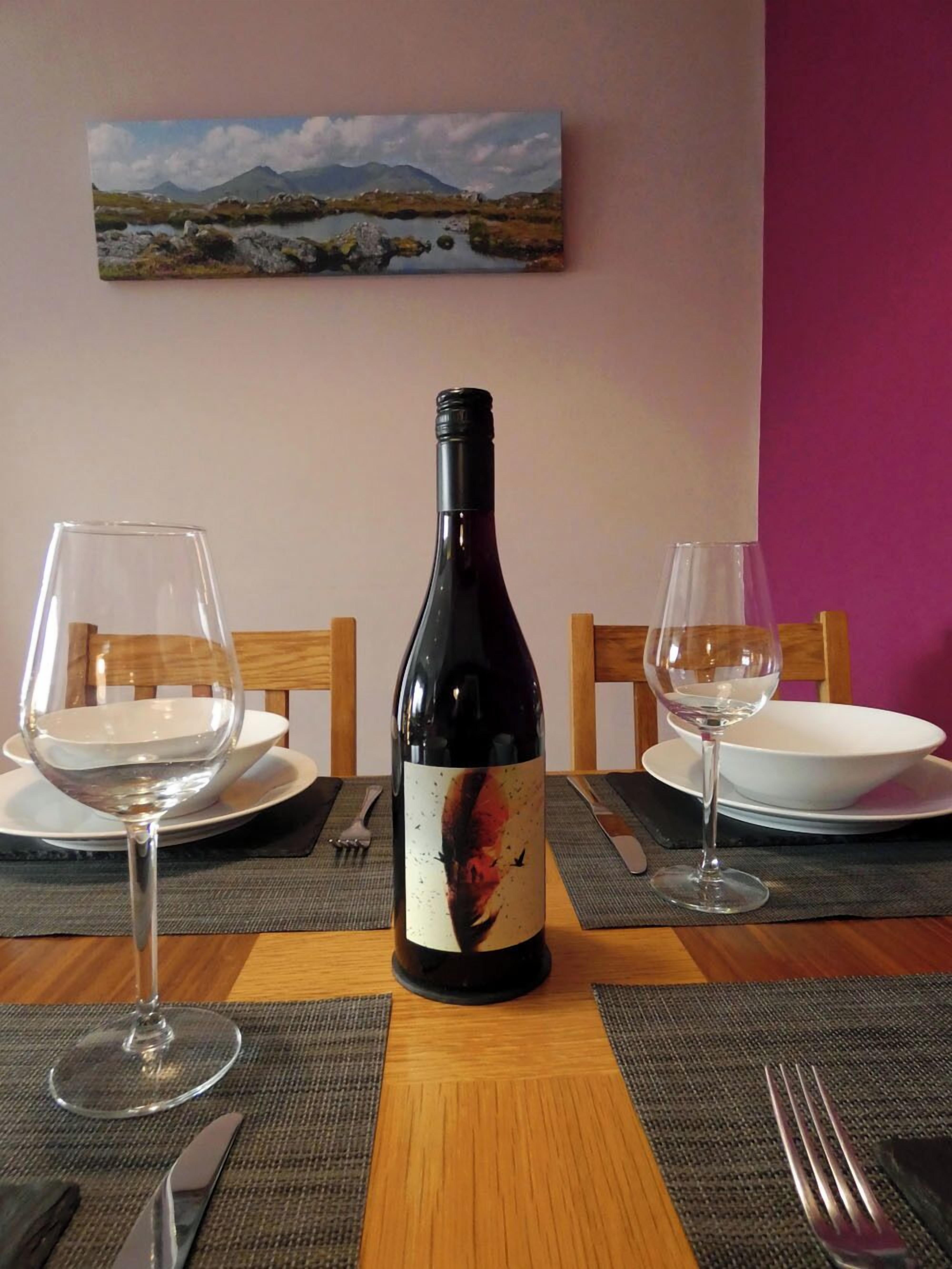 Une table à manger avec une bouteille de vin, deux verres à vin et un tableau accroché au mur.