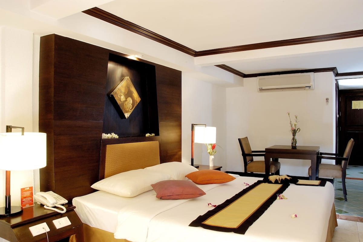 A hotel room with a bed, bedside table, lamp, and a small table with chairs.