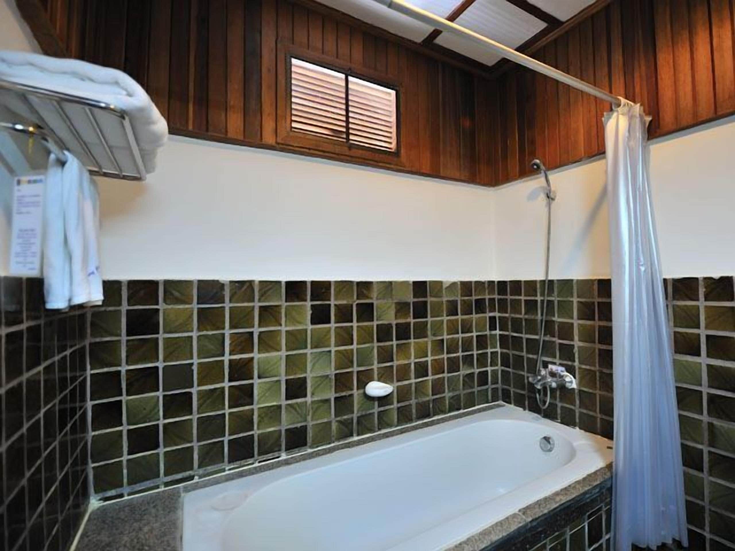 Une salle de bain avec une baignoire, une douche et une fenêtre équipée de stores.