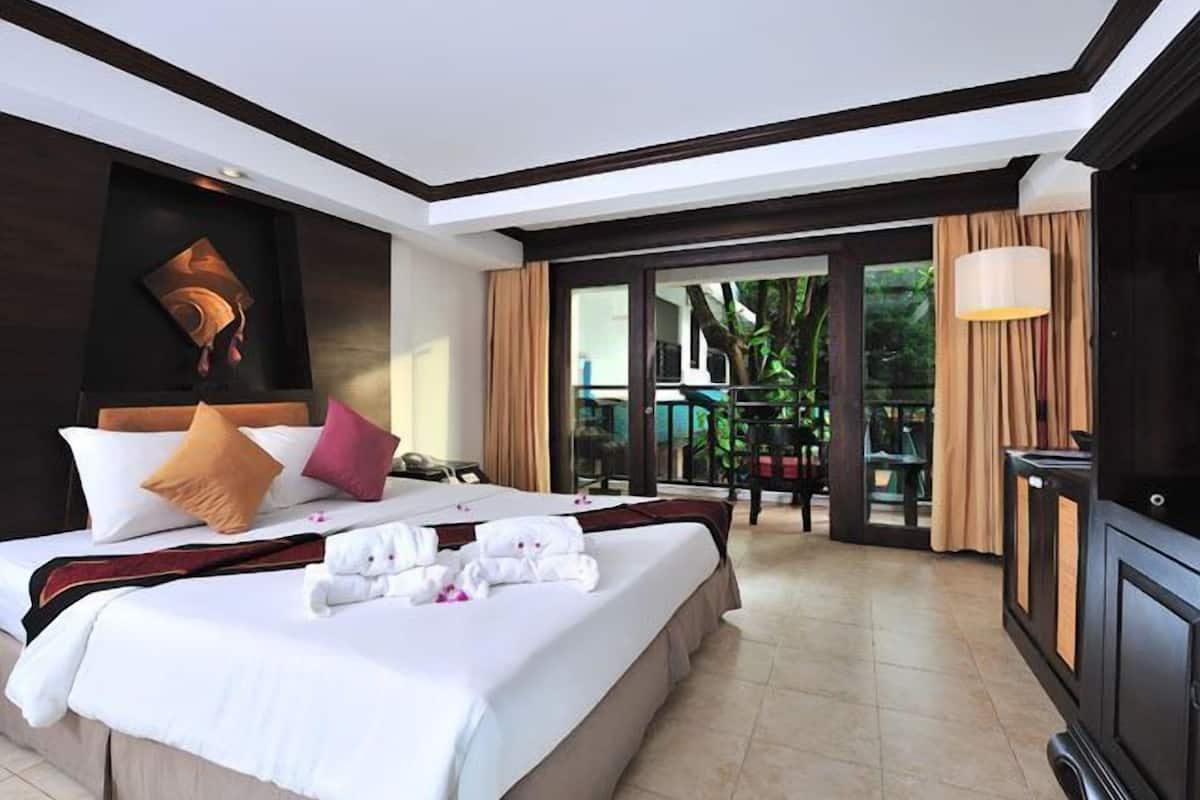 A hotel room with a large bed, a TV, and a balcony with a view of greenery.