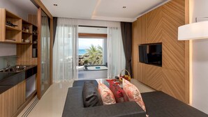 A modern living room with a sofa, a TV mounted on the wall, and a view of the ocean through large windows. - Kudo Hotel (Patong)