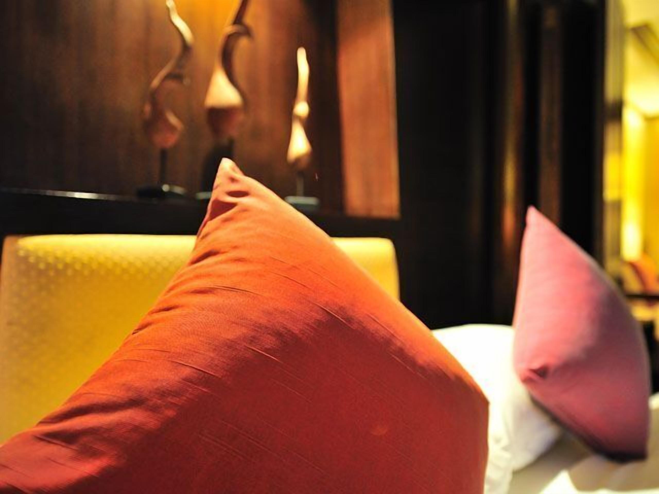 A hotel room with a bed, pillows, and a wooden headboard.