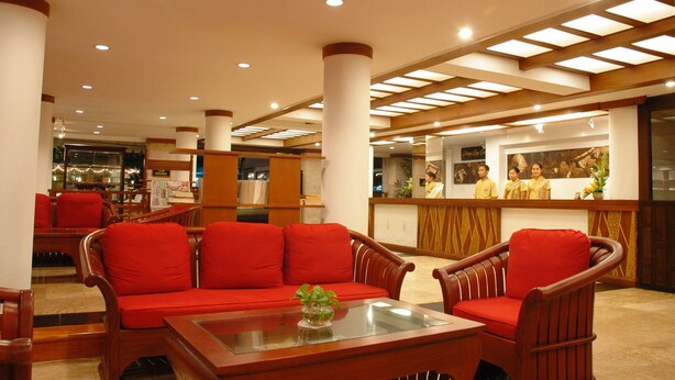 A hotel lobby with red cushioned seating, a reception desk, and a glass coffee table with a plant. - Kudo Hotel (Patong)
