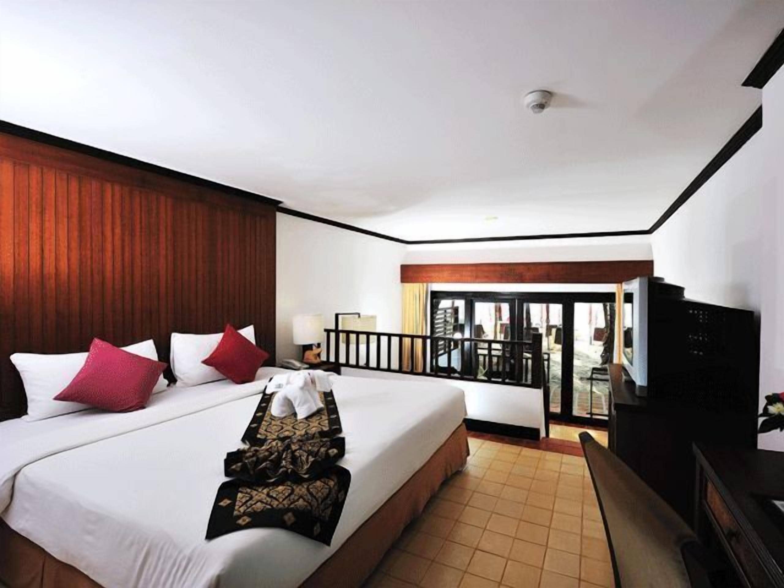 A hotel room with a large bed, a TV, a balcony, and a view of the outside.