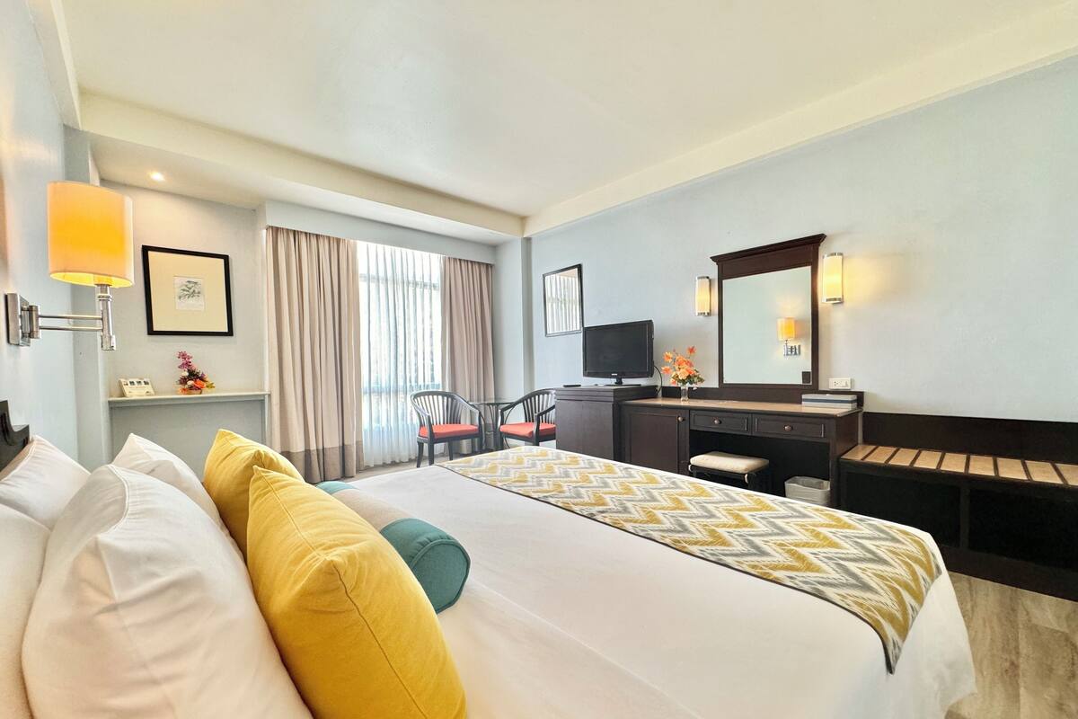 A hotel room with a bed, a desk, a chair, a TV, and a large window with curtains.