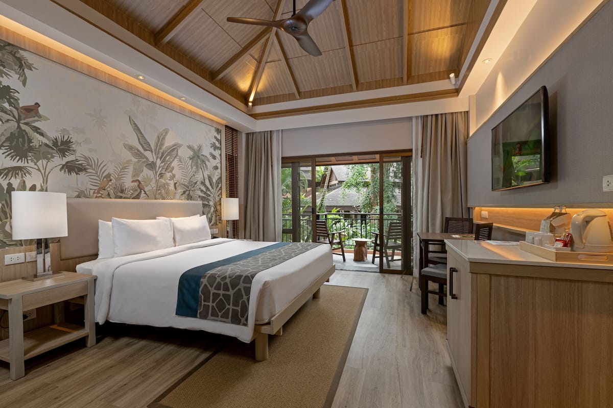 Une chambre d’hôtel avec un grand lit, un bureau, un ventilateur de plafond et une vue sur l’extérieur.