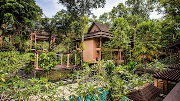 A resort with a swimming pool surrounded by lush greenery and a building with a traditional roof.