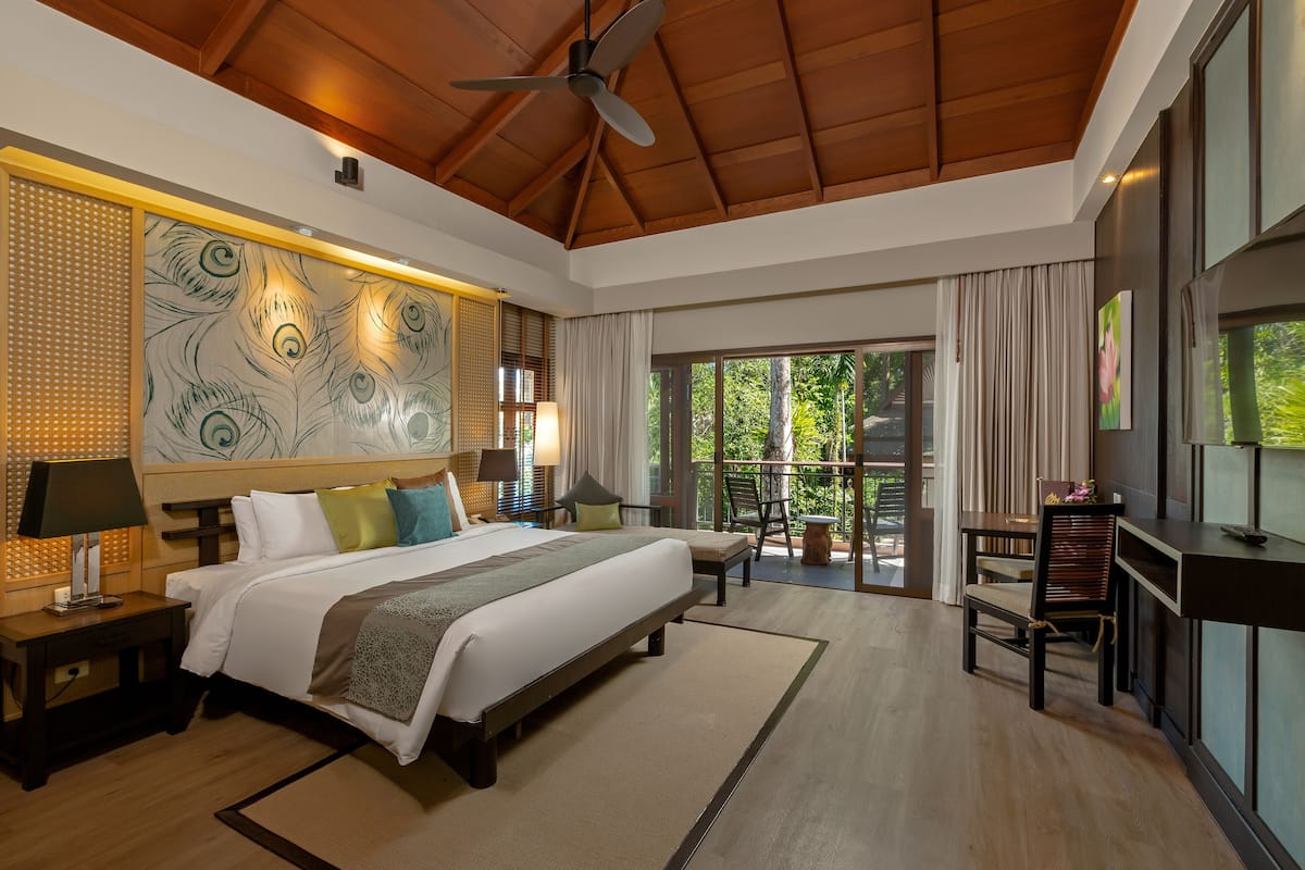 Une chambre spacieuse avec un grand lit, un ventilateur de plafond et un balcon offrant une vue sur la verdure.