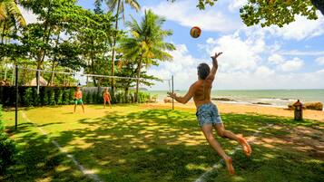 A beach volleyball game on a grassy area with palm trees and ocean views.
