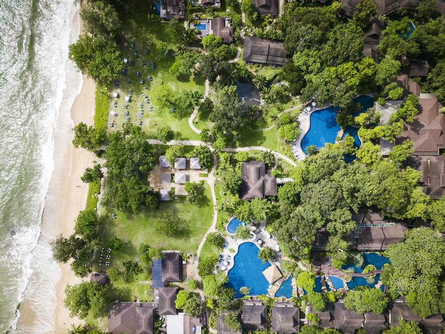 Een luchtbeeld van een resort met meerdere zwembaden, een strand en weelderige begroeiing.
