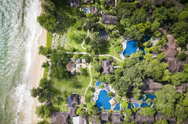 Vista aérea de un resort con múltiples piscinas, una playa y abundante vegetación.