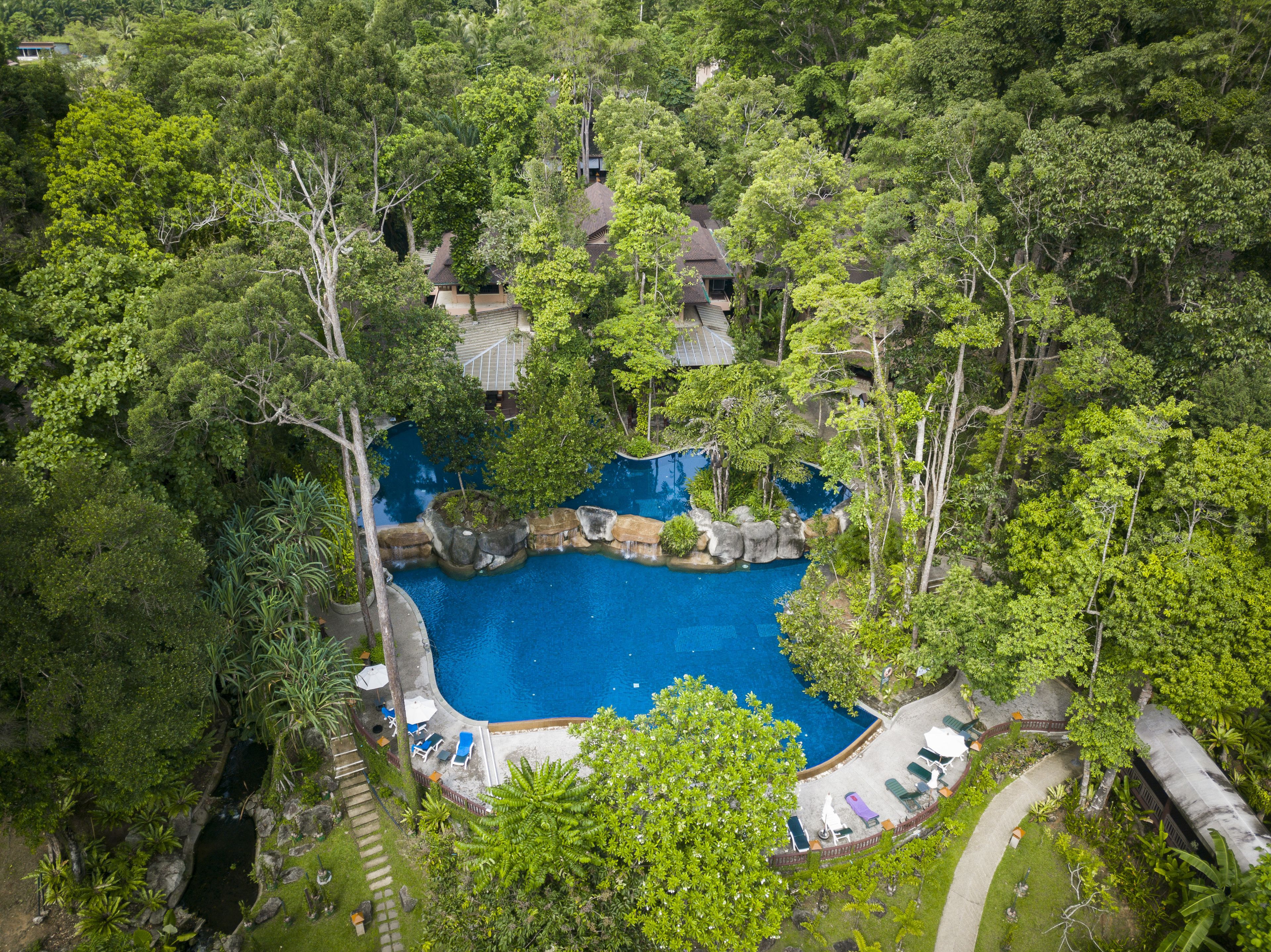 An aerial view of a resort with a central swimming pool surrounded by lush greenery and multiple bungalow-style buildings.
