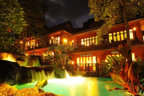 Un hotel con cascada, piscina y fachada bien iluminada.