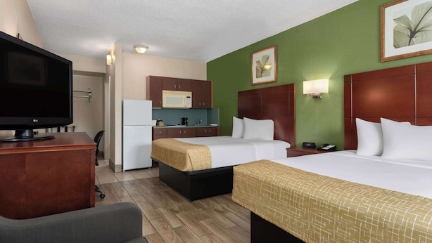 Une chambre d’hôtel avec deux lits, un bureau avec une télévision, un coin cuisine et un mur d’accent de couleur verte.