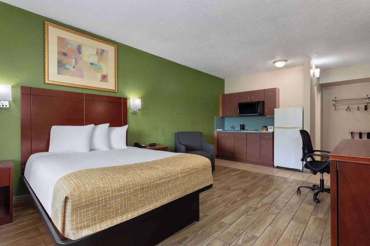 A hotel room with a bed, a desk, a chair, a kitchenette, and a bathroom.