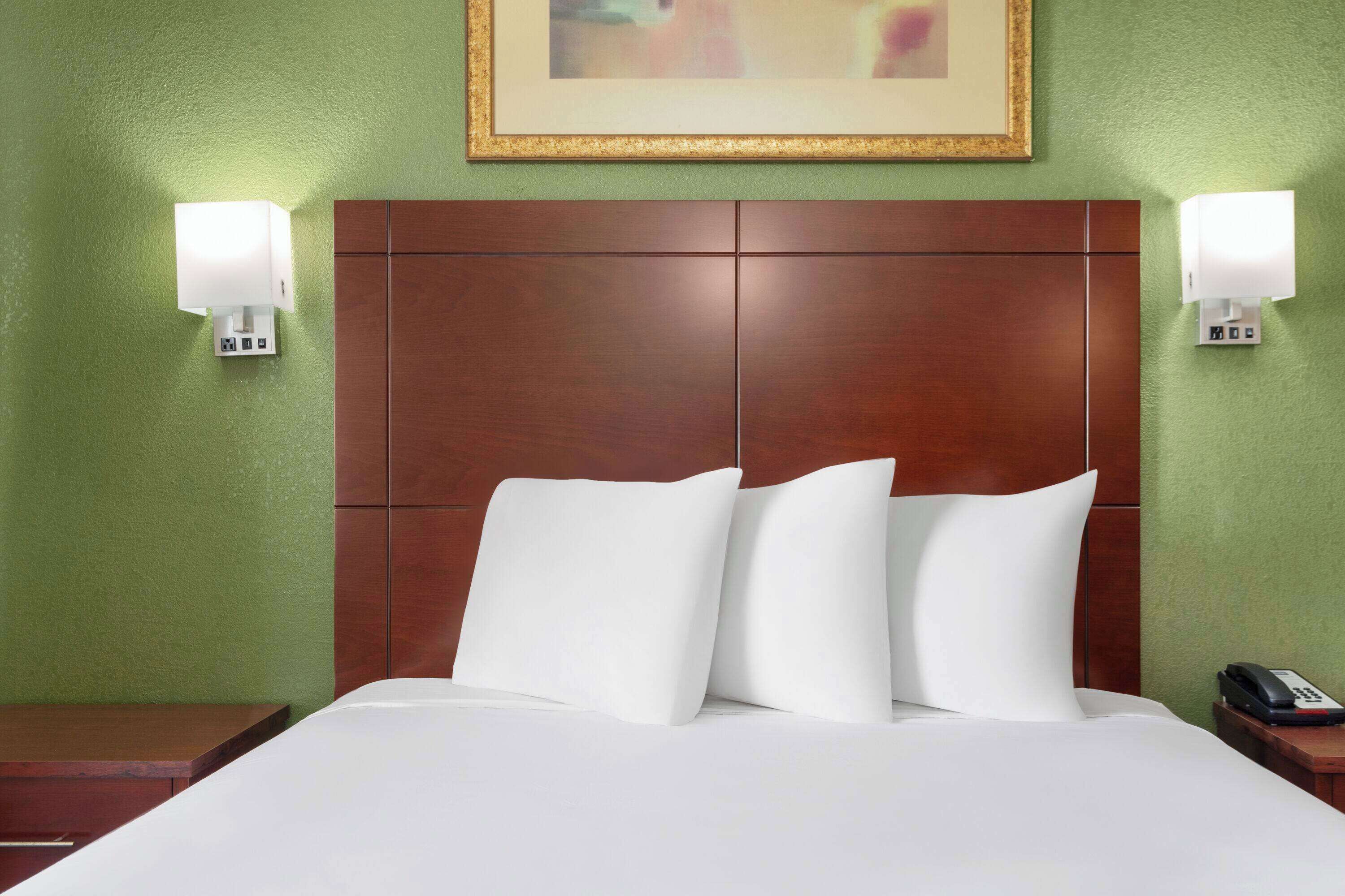 A hotel room with a large bed, two bedside tables, a wooden headboard, and wall-mounted lamps.