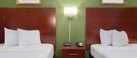 A hotel room with two beds, a nightstand with a clock and phone, and framed botanical artwork on the green walls.