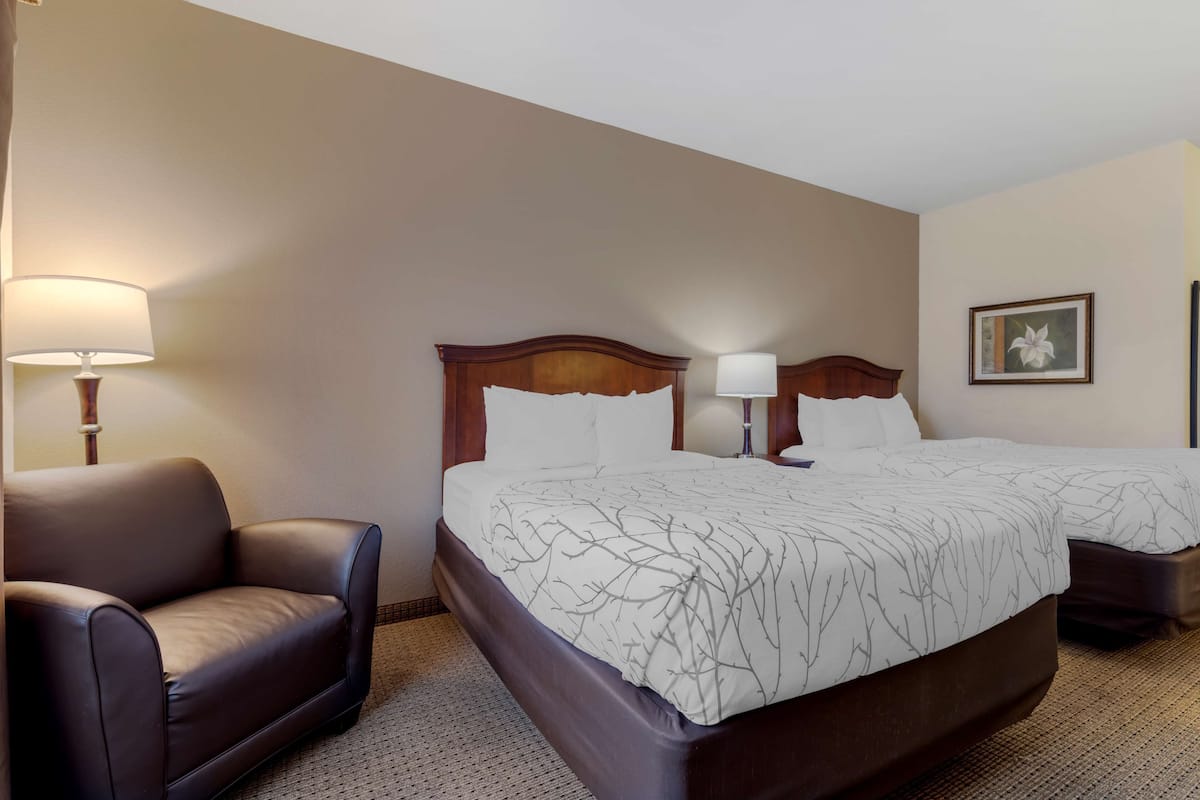 Una habitación de hotel con una cama grande, dos mesitas de noche, una silla y una lámpara.