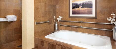 A bathroom with a bathtub, a handrail, a towel rack, and a framed picture on the wall.
